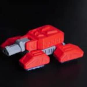 May include: A red and gray toy vehicle with a futuristic design. The toy has a main body with angular shapes and two smaller, wing-like structures on the sides. The vehicle is set against a dark background.