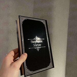 Peut inclure: Un livre reli&eacute; noir avec une bordure argent&eacute;e et le nom de l'auteur, "Stephenie Meyer", imprim&eacute; en lettres argent&eacute;es.