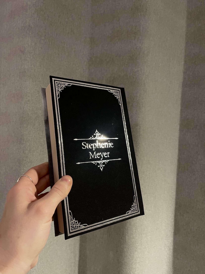 Peut inclure: Un livre reli&eacute; noir avec une bordure argent&eacute;e et le nom de l'auteur, "Stephenie Meyer", imprim&eacute; en lettres argent&eacute;es.