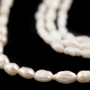 May include: A strand of white oval pearls, strung together to form a necklace. The pearls are smooth and lustrous, and the necklace is draped over a black surface.
