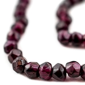 May include: A strand of dark purple gemstone beads. The beads are faceted and have a slightly irregular shape. The beads are strung on a clear thread.