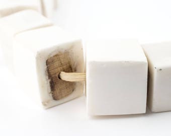 May include: A white ceramic bracelet with wooden beads and a natural fiber string connecting the beads.