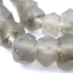May include: Close-up of a strand of faceted, translucent beads. The beads are a soft, muted grey colour and have a rough, textured surface. Each bead is hexagonal in shape. The beads are strung together, suggesting they are for jewellery making.