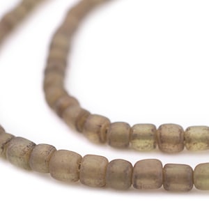 May include: Close-up of two strands of olive-green, square-shaped beads. The beads have a slightly matte finish and are strung together, creating a necklace or bracelet component. The background is plain white.