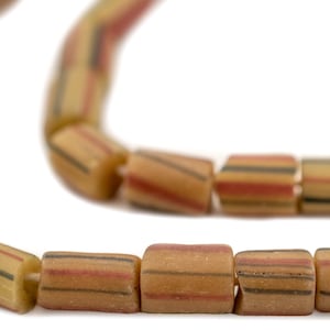May include: A strand of rectangular beads with a tan base color and horizontal stripes of red, black, and green. The beads are strung together, creating a curved line against a white background. The beads are likely made of glass or a similar material.