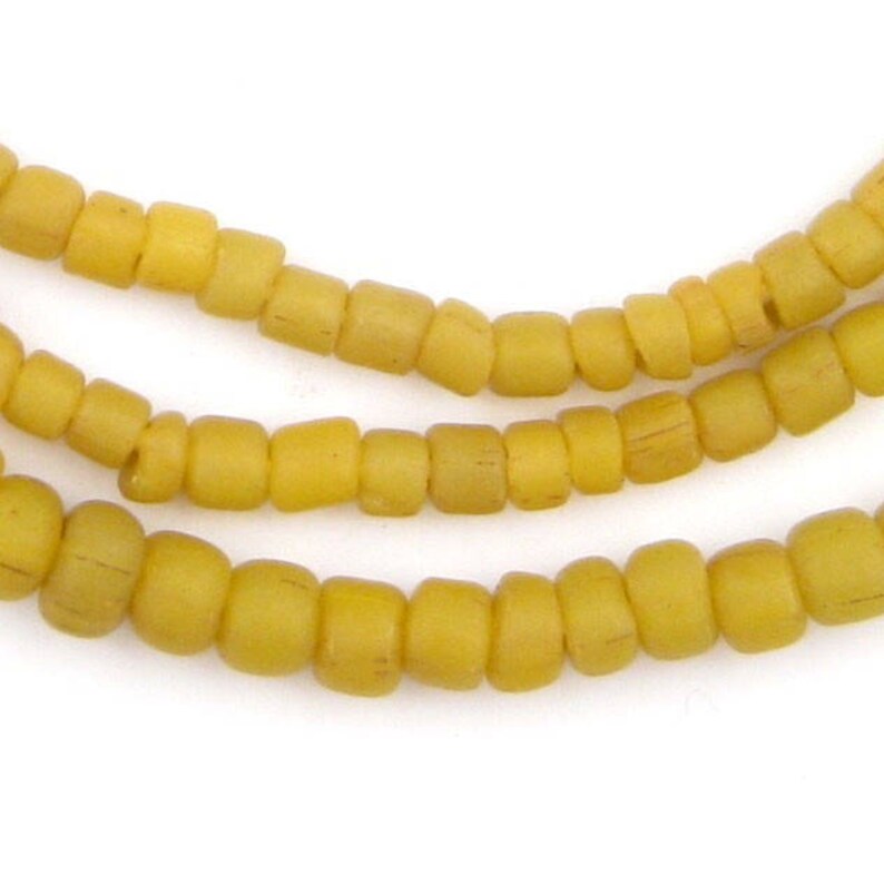 May include: A strand of yellow glass beads. The beads are small and round, and they have a slightly matte finish.