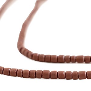 May include: A close-up of a brown necklace with small, square beads. The necklace is made of a series of connected, evenly spaced beads. The background is plain white.