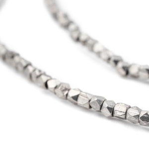 May include: A silver necklace made of small, faceted beads. The beads are linked together to form a chain.