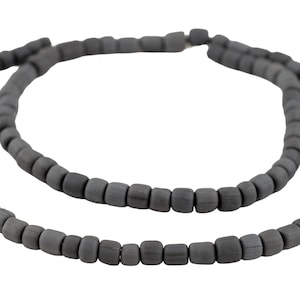 以下が含まれることがあります： 濃い灰色のビーズネックレスの2つのストランド。ビーズは小さく、正方形で、ネックレスの長さに沿って均等に配置されています。ネックレスは白い背景に表示され、ビーズの色と質感を強調しています。