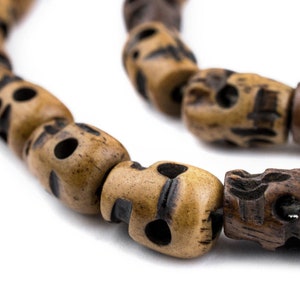 May include: A close-up of a brown wooden necklace with skull-shaped beads. The beads are carved with intricate details and have a natural, rustic look.