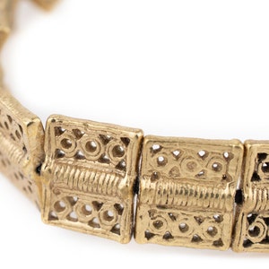 May include: Close-up of a gold-colored bracelet. The bracelet is made of rectangular links with intricate circular and linear patterns. The links are connected to form a flexible chain.