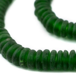 May include: A strand of dark green, disc-shaped beads. The beads are strung together, forming a curved line against a white background. The beads have a slightly irregular shape and a matte finish.