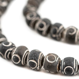 May include: A black and white beaded necklace with a repeating pattern of circles and lines. The beads are made of a smooth, polished material.