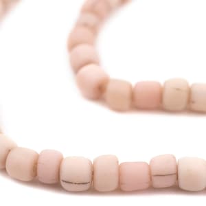 Op de afbeelding: Close-up van een streng lichtroze, vierkante kralen. De kralen hebben een enigszins onregelmatige vorm en een matte afwerking. De kralen zijn aan elkaar geregen, waardoor een ketting of armband ontstaat.