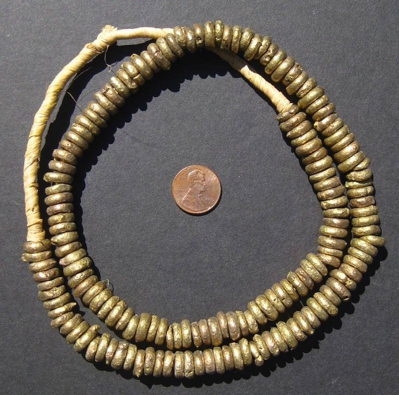May include: A gold necklace made of small, round beads. The beads are strung on a white cord. The necklace is approximately 50 cm long.