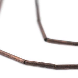 Pu&ograve; includere: Un primo piano di una collana di perline di legno marrone. Le perline sono cilindriche e hanno una finitura liscia e opaca.