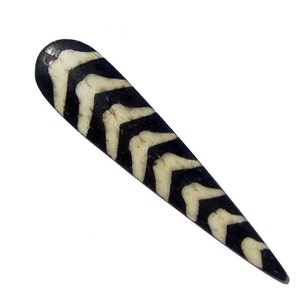 May include: A black and white bone pendant with a chevron pattern. The pendant has a hole at the top for hanging.