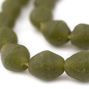 Pode incluir: Close-up de um fio de contas verde-oliva. As contas têm uma forma facetada e irregular e um acabamento fosco. As contas são enfiadas em um fio branco e o fundo é branco.