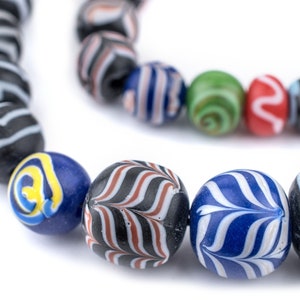 Könnte beinhalten: Nahaufnahme einer bunten Glasperlenkette. Die Perlen sind rund und haben verschiedene Muster, darunter Streifen, Spiralen und Zickzackmuster. Die Perlen sind in Blautönen, Schwarz, Weiß, Rot und Grün.