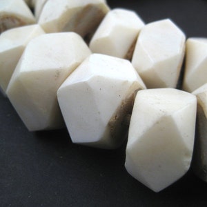 May include: A close-up of a white bone bead necklace. The beads are faceted and have a slightly irregular shape. The necklace is made of natural bone and has a rustic, organic look.
