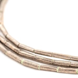 Puede incluir: Un collar de plata con múltiples hileras de cuentas cilíndricas. Las cuentas tienen una superficie texturizada y están separadas por pequeños separadores verdes.