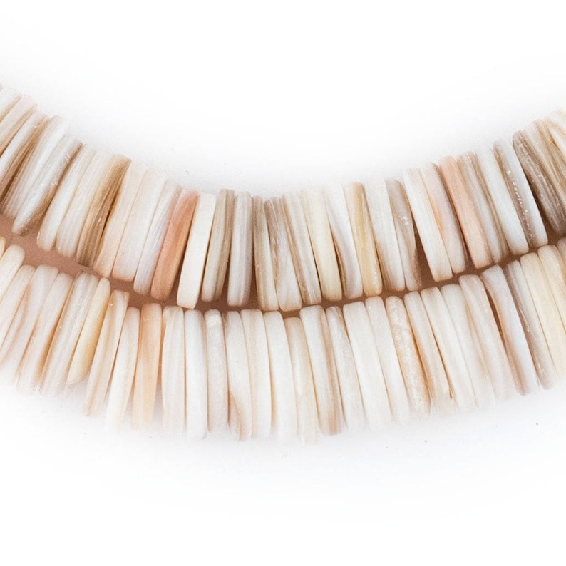 May include: Close-up of a necklace made of rectangular, off-white beads with subtle variations in color, including hints of beige and peach. The beads are arranged in two parallel strands, creating a curved shape against a white background.