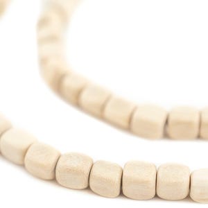 May include: Close-up of a necklace made of light beige wooden beads. The beads are square-shaped and strung together, creating a curved line against a white background. The necklace appears to be handmade.