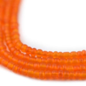 May include: Close-up of several strands of orange glass beads. The beads are small, round, and have a matte finish. The strands are curved, creating a flowing, organic shape against a white background. The beads are a vibrant, warm orange colour.
