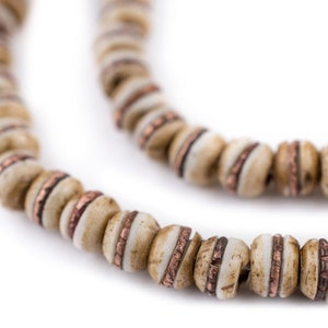 May include: A close-up of a necklace made of beige and copper beads. The beads are round and have a smooth, polished finish. The necklace is strung on a thin cord.