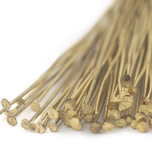 Puede incluir: Primer plano de un montón de alfileres de cabeza dorados. Los alfileres están dispuestos en forma de abanico, con las cabezas de los alfileres mirando al espectador.