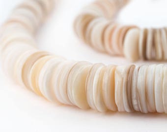 Op de afbeelding: Een close-up van een ketting gemaakt van platte, ronde schelpkralen. De kralen hebben tinten van crème, beige en lichtbruin. De ketting is gebogen, met de kralen in een cirkelvormig patroon tegen een witte achtergrond.