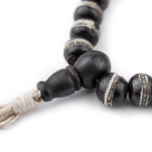 May include: A black and white beaded necklace with a white tassel. The beads are round and have a silver trim.