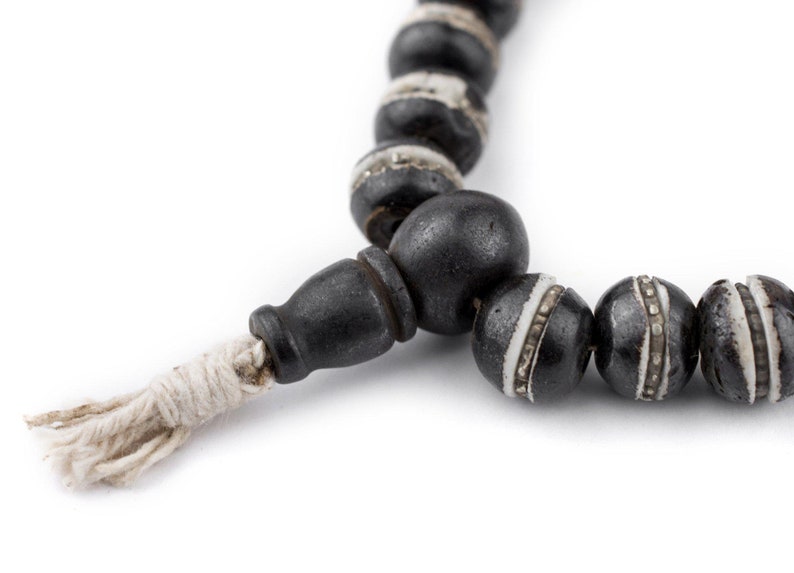 May include: A black and white beaded necklace with a white tassel. The beads are round and have a silver trim.