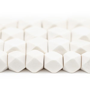 Puede incluir: Primer plano de una fila de cuentas de cerámica blanca con forma geométrica facetada. Las cuentas están dispuestas en un patrón escalonado, creando una textura visualmente interesante.