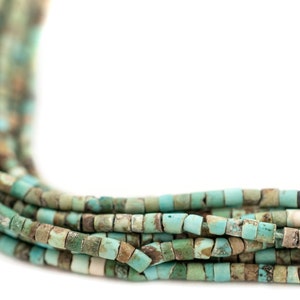 May include: Close-up of strands of turquoise-colored beads. The beads are small, square-shaped, and have a mix of blue, green, and brown hues. The beads are strung together, creating a textured and layered effect.