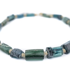 May include: A necklace made of blue and green glass beads. The beads are cylindrical and have a rough, textured surface. The necklace is strung on a white cord.
