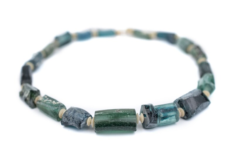 May include: A necklace made of blue and green glass beads. The beads are cylindrical and have a rough, textured surface. The necklace is strung on a white cord.