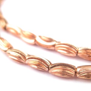 May include: A strand of copper-colored beads with a wavy, ribbed design. The beads are strung together to form a necklace or bracelet.