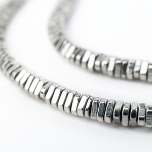 May include: A silver necklace made of small, hexagonal-shaped beads. The beads are linked together to form a continuous chain.