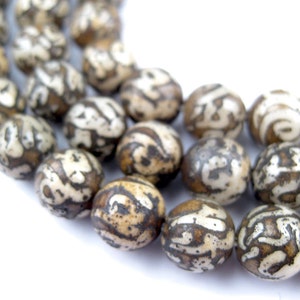 May include: A strand of brown and white patterned beads. The beads are oval shaped and have a natural, organic look.