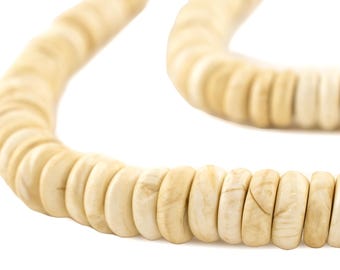 Op de afbeelding: Een close-up van een ketting gemaakt van lichtbeige, afgeronde kralen. De kralen zijn aan elkaar geregen en vormen een gebogen vorm tegen een witte achtergrond. De ketting lijkt gemaakt van natuurlijke materialen.