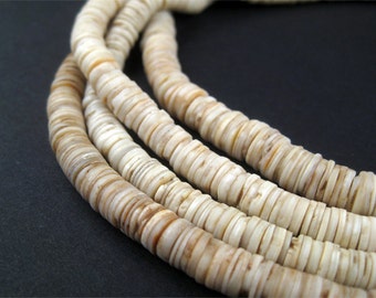 May include: Close-up of several strands of off-white, disc-shaped beads. The beads have a natural, organic appearance with subtle variations in color, ranging from cream to light brown. The beads are strung together, creating a layered effect.