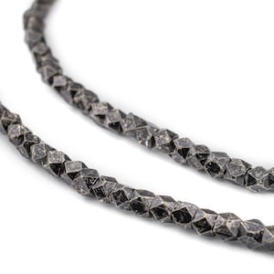 May include: A close-up of a silver necklace with faceted beads. The beads are a dark gray color and have a textured surface.