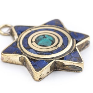 Peut inclure: Un pendentif en forme d'étoile à six branches de couleur dorée avec une incrustation bleue et verte. Le centre de l'étoile présente un motif circulaire avec une pierre verte entourée d'une mosaïque bleue.