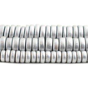 May include: A close-up of a strand of silver-colored wooden beads. The beads are round and have a smooth, polished finish.