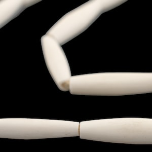 May include: A strand of white bone beads, each bead is cylindrical and slightly curved. The beads are strung together to form a necklace.