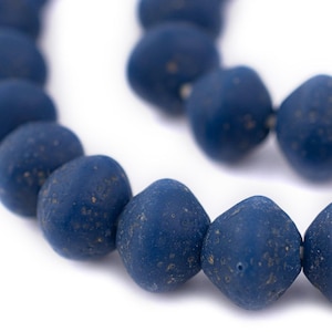 May include: Close-up of a strand of dark blue beads. The beads have a matte finish and a slightly irregular shape, with small flecks of a lighter color. The beads are strung together, creating a necklace or bracelet.