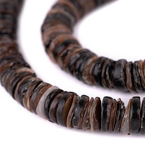 May include: Close-up of a necklace made of flat, round, dark brown and black beads. The beads have a natural, organic appearance, with variations in color and texture. The necklace is displayed against a white background.