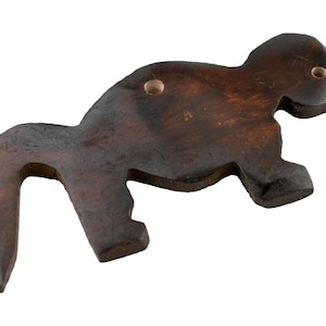 May include: A dark brown, wooden monkey-shaped bottle opener. The opener has a hook-like tail and two small holes near the head. The wood grain is visible, and the opener is designed to sit flat.