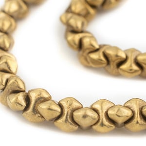 May include: Close-up of a strand of golden-colored beads. Each bead has a unique, textured shape with a slightly pointed design. The beads are strung together, creating a curved line against a white background. The overall aesthetic is vintage or antique.